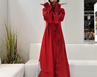 Könnte beinhalten: Eine Frau trägt ein langes, rotes, Kapuzenkleid mit einem einzigartigen Design. Das Kleid hat einen gerafften Ausschnitt und einen langen, fließenden Rock. Das Kleid ist aus einem weichen, bequemen Stoff.