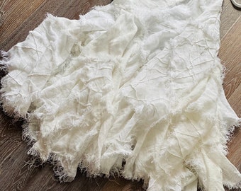 May include: White linen skirt with a frayed hem. The skirt is gathered and has a loose, flowing fit.