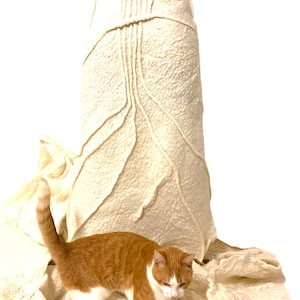 May include: A white felted skirt with a unique design. The skirt is long and flowing, with a gathered waistband. A cat is sitting on the skirt.