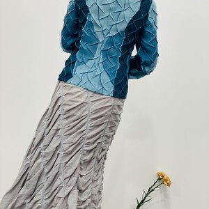 May include: A blue denim jacket with a unique quilted design. The jacket has a stand-up collar and long sleeves.