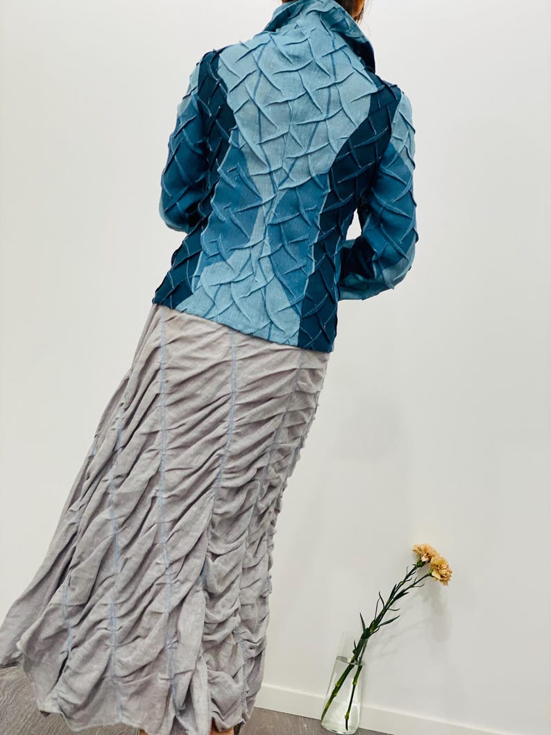 May include: A blue denim jacket with a unique quilted design. The jacket has a stand-up collar and long sleeves.
