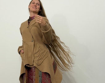 Peut inclure: Veste asymétrique de couleur beige avec des coutures originales et une fermeture boutonnée. La veste est associée à une longue jupe à motifs dans les tons de rouge, vert et or. La personne a de longs cheveux flottants.