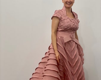 May include: A woman wearing a pink dress with a ruffled skirt and a belt. The dress has a textured fabric and a short sleeve design.