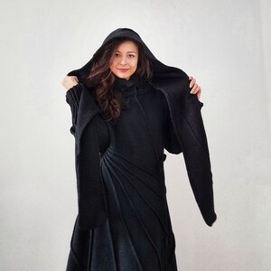 May include: A black hooded sweater dress with long sleeves and a fitted silhouette. The dress has a unique design with diagonal lines and a high neckline.