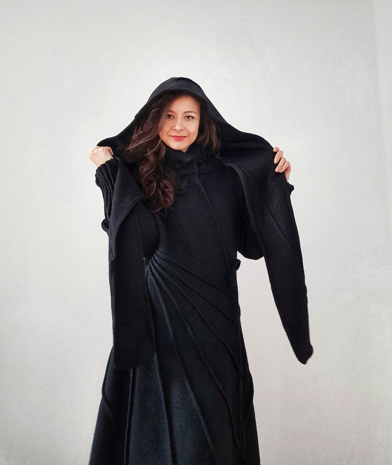 May include: A black hooded sweater dress with long sleeves and a fitted silhouette. The dress has a unique design with diagonal lines and a high neckline.
