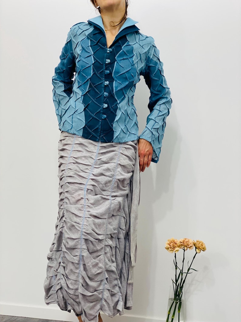 May include: A blue and teal textured jacket with a button-up front and long sleeves. The jacket is paired with a long, flowing, grey skirt.