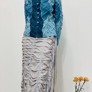 May include: A blue and teal patterned button-up shirt with long sleeves and a collar. The shirt is made of a textured fabric and has a unique design.