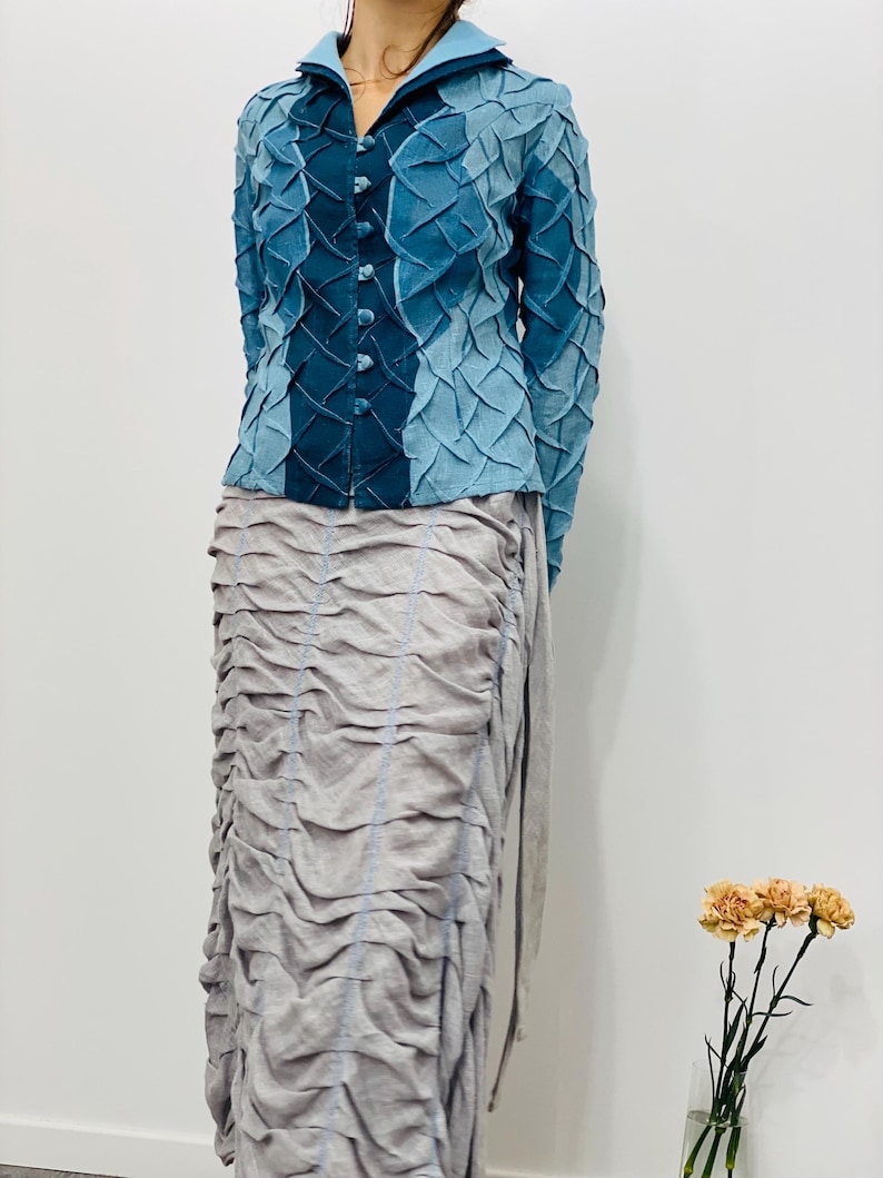 May include: A blue and teal patterned button-up shirt with long sleeves and a collar. The shirt is made of a textured fabric and has a unique design.