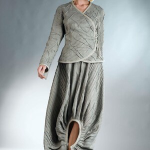 May include: A woman wearing a gray, textured, wrap-style top and a matching skirt with a unique, gathered design. The skirt has a large, open circle in the front, revealing her leg.