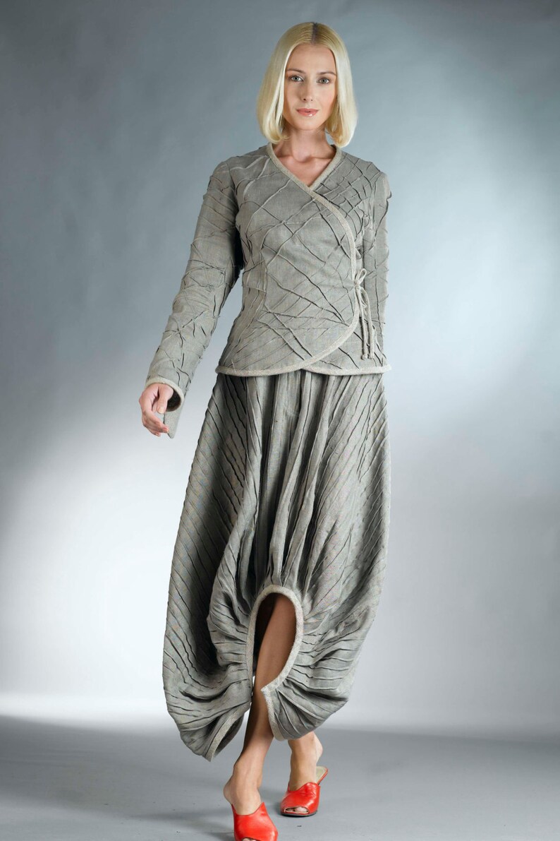 May include: A woman wearing a gray, textured, wrap-style top and a matching skirt with a unique, gathered design. The skirt has a large, open circle in the front, revealing her leg.