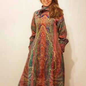 May include: A long, flowing dress with a paisley pattern in shades of red, blue, green, and gold. The dress has a high neck and long sleeves.