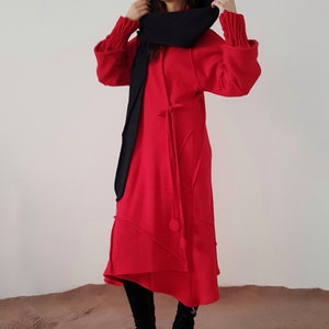 May include: A red hooded dress with a black scarf. The dress has a long, flowing skirt and a cinched waist. The model is wearing black boots.