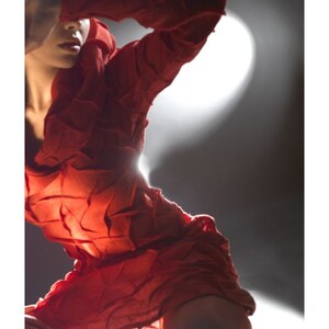 Peut inclure: Une femme portant une robe rouge textur&eacute;e pose avec une main qui couvre son visage. La robe est faite d'un tissu qui semble &ecirc;tre compos&eacute; de nombreuses petites pi&egrave;ces cousues ensemble.
