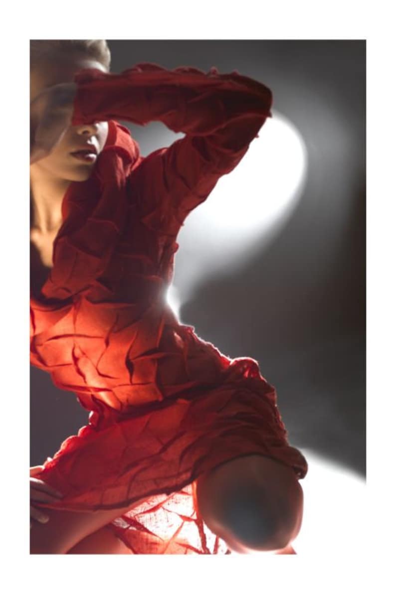 Peut inclure: Une femme portant une robe rouge textur&eacute;e pose avec une main qui couvre son visage. La robe est faite d'un tissu qui semble &ecirc;tre compos&eacute; de nombreuses petites pi&egrave;ces cousues ensemble.