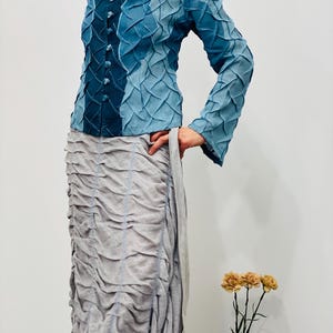 May include: A blue denim jacket with a textured, quilted design. The jacket has a collar, long sleeves, and a button closure.