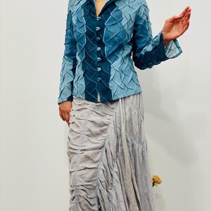 May include: A blue denim jacket with a textured, quilted design. The jacket has a collar and long sleeves. The jacket is buttoned up the front.