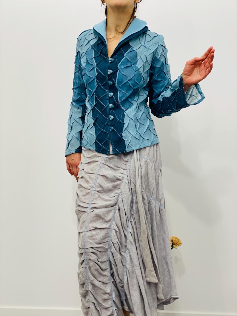 May include: A blue denim jacket with a textured, quilted design. The jacket has a collar and long sleeves. The jacket is buttoned up the front.