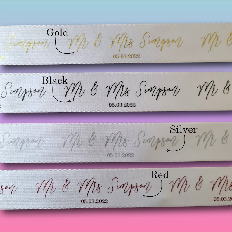 May include: White satin ribbons with gold, black, silver, and red text. The ribbons display the names "Mr & Mrs Simpson" and the date "05.03.2022" in a cursive font, ideal for wedding decorations.