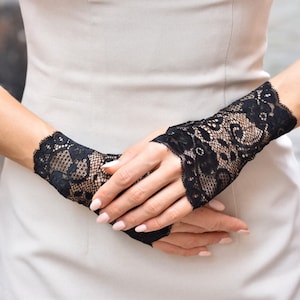 Puede incluir: Un par de guantes sin dedos de encaje negro con un patr&oacute;n floral.