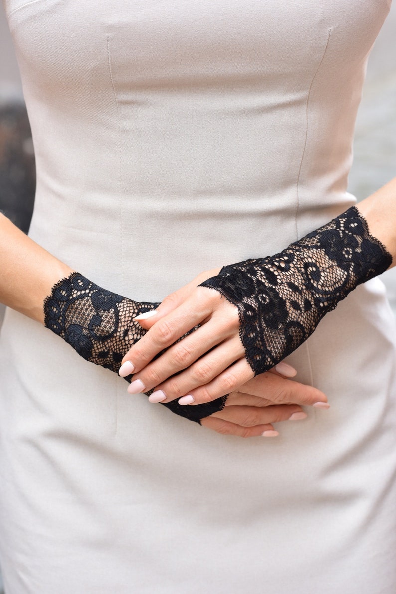 Puede incluir: Un par de guantes sin dedos de encaje negro con un patr&oacute;n floral.