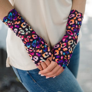 May include: A pair of fingerless gloves with a colorful leopard print on a black background. The gloves are made of a sheer, mesh fabric.