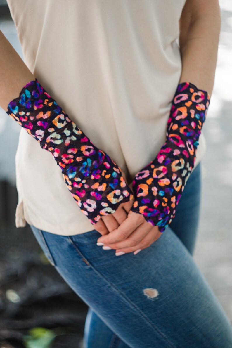 May include: A pair of fingerless gloves with a colorful leopard print on a black background. The gloves are made of a sheer, mesh fabric.