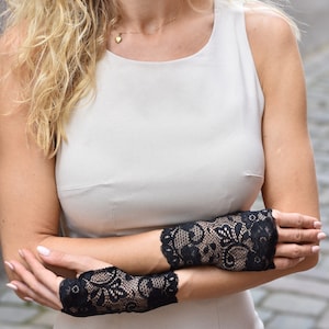Puede incluir: Una mujer con un vestido blanco sin mangas y guantes sin dedos de encaje negro. Los guantes tienen un patr&oacute;n floral.
