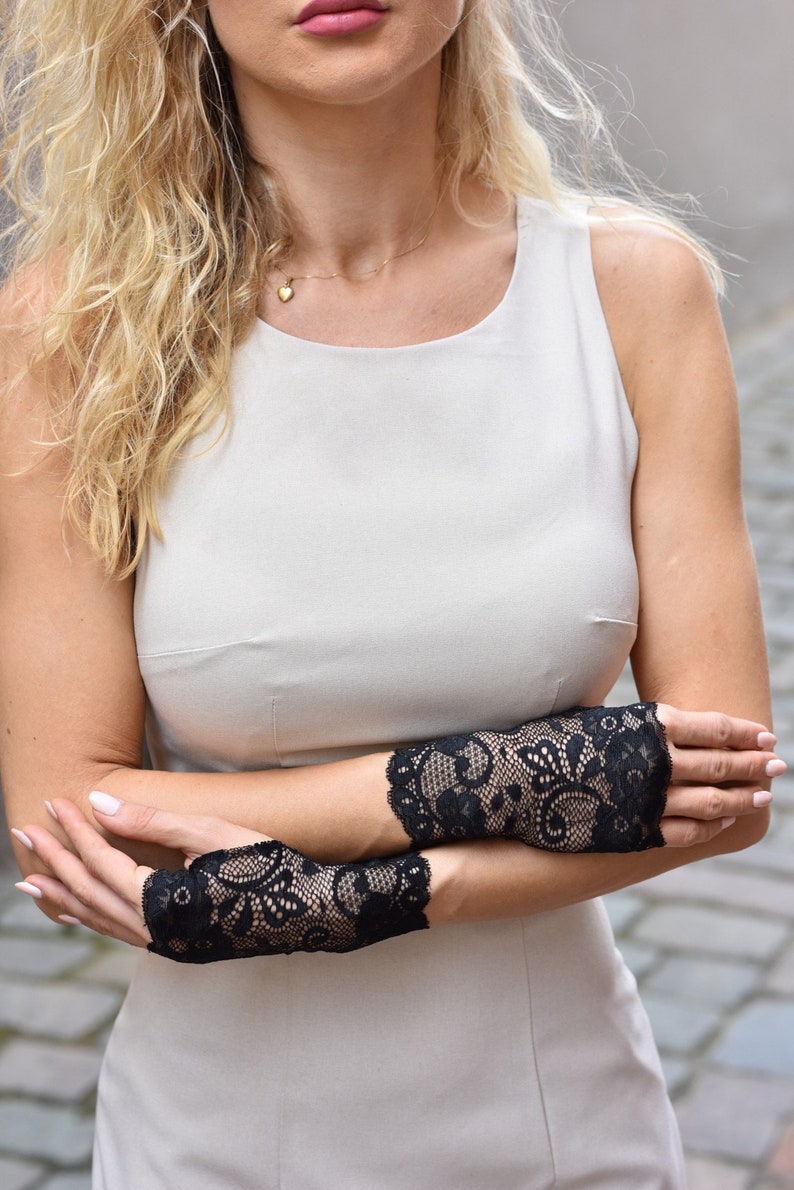 Puede incluir: Una mujer con un vestido blanco sin mangas y guantes sin dedos de encaje negro. Los guantes tienen un patr&oacute;n floral.