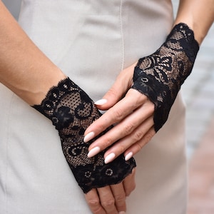 Puede incluir: Un par de guantes sin dedos de encaje negro con un delicado patr&oacute;n floral. Los guantes se llevan en las manos de una persona, con las yemas de los dedos expuestas.