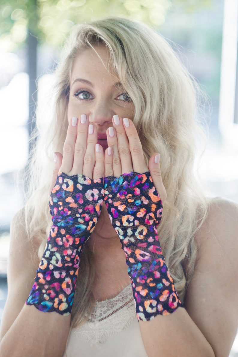 May include: A woman wearing a pair of black fingerless gloves with a colorful leopard print design. The gloves are made of a sheer, mesh fabric.