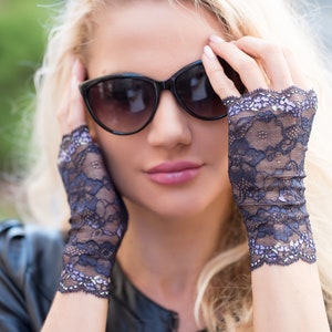 May include: Black cat-eye sunglasses and dark blue lace fingerless gloves. The gloves have a delicate floral pattern with lavender accents. The woman is wearing a black leather jacket.