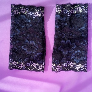 May include: Two black lace arm warmers with a floral pattern and a scalloped edge. The lace has a dark blue and purple floral design. The top edge has a white and yellow floral pattern.