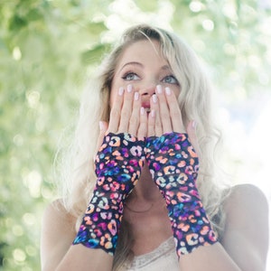 May include: A woman with blonde hair is wearing a pair of colorful fingerless gloves with a leopard print pattern. The gloves are made of a sheer fabric and have a black base with pink, blue, and orange accents.