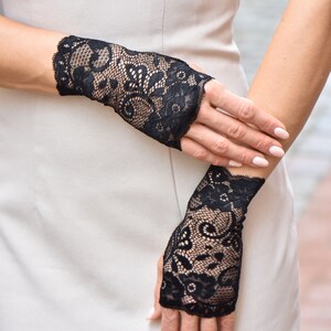 Puede incluir: Un par de guantes sin dedos de encaje negro con un patr&oacute;n floral. Los guantes se llevan en ambas manos.