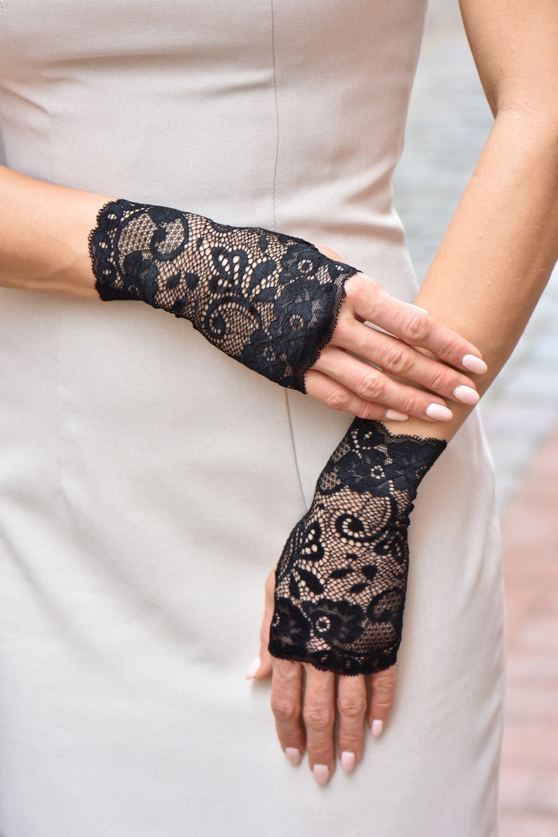 Puede incluir: Un par de guantes sin dedos de encaje negro con un patr&oacute;n floral. Los guantes se llevan en ambas manos.