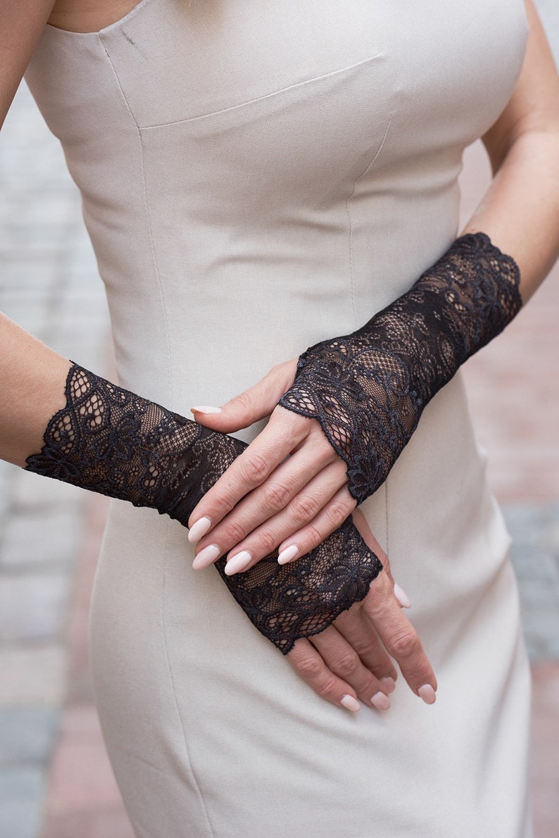 May include: A pair of black lace fingerless gloves with a delicate floral pattern. The gloves are worn on a person's hands, with the fingertips exposed.