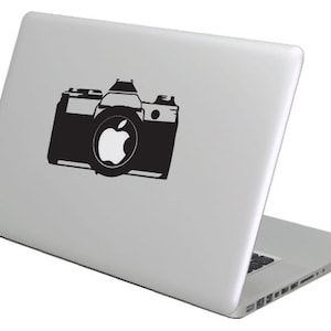 Op de afbeelding: Een zilveren laptop met een zwarte camera sticker op de deksel. De camera sticker heeft een apple logo in het midden.