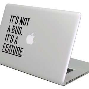 Peut inclure: Un ordinateur portable argenté avec un autocollant noir qui dit "Ce n'est pas un bug, c'est une fonctionnalité".