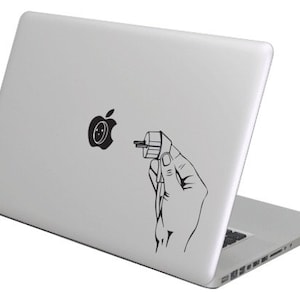 May include: A silver laptop with a black sticker on the back. The sticker shows a hand holding a plug with the apple logo in the socket.
