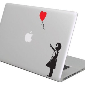 Puede incluir: Un portátil plateado con una silueta en blanco y negro de un niño que alcanza un globo rojo en forma de corazón. El portátil tiene un logotipo de Apple en la parte posterior.