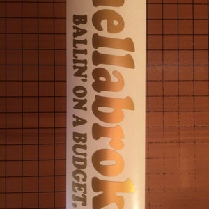 May include: Gold vinyl sticker with the text "hellabroke BALLIN' ON A BUDGET."