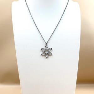 K&ouml;nnte beinhalten: Silberfarbene Halskette mit einem filigranen, sechszackigen Blumenanh&auml;nger. Der Anh&auml;nger h&auml;ngt an einer feinen Kette. Die Halskette wird auf einer wei&szlig;en B&uuml;ste vor neutralem Hintergrund pr&auml;sentiert.