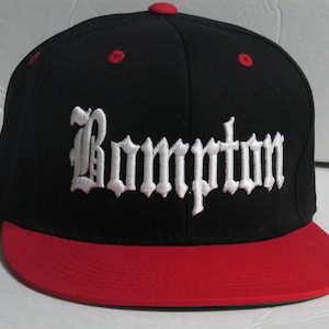 May include: Black and red baseball cap with a white embroidered "Compton" in old English lettering.