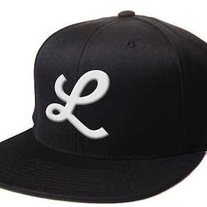 May include: A black and white baseball cap with a white embroidered letter "L" on the front.