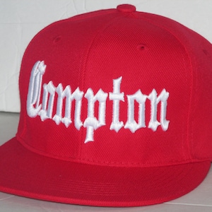 May include: Red baseball cap with a white embroidered "Compton" in old English lettering.