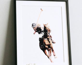 May include: Framed print of a polo match in action. The artwork depicts a polo player in a helmet and dark attire, swinging a mallet while riding a brown horse. The print is set in a black frame.