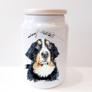 May include: White ceramic dog treat jar with a wooden lid. The jar features a watercolour illustration of a Bernese Mountain Dog with the words "woof treats" written in black cursive.