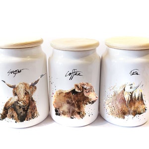 Pu&ograve; includere: Set di tre barattoli in ceramica bianca con coperchi in legno. Ogni barattolo presenta un'illustrazione ad acquerello di una mucca delle Highlands e le parole "Zucchero", "Caff&egrave;" e "T&egrave;".