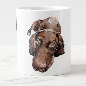 May include: White ceramic mug featuring a watercolor illustration of a brown dog with expressive eyes. The dog's head and part of its body are depicted, showcasing its fur and facial features. A charming and artistic design for dog lovers.