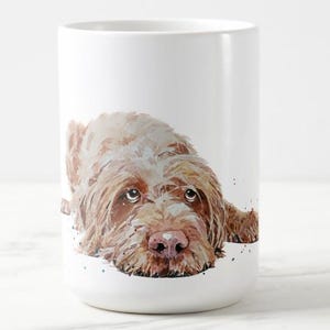 May include: White ceramic mug featuring a watercolor illustration of a brown and white dog with a pink nose. The dog is lying down, with its head resting on the surface. The mug has a glossy finish and a simple, cylindrical shape.